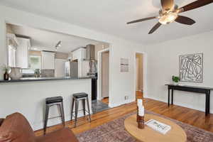Kitchen featuring freestanding refrigerator, wall chimney exhaust hood, light wood finished floors, white cabinets, and dark countertops