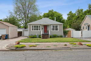 Bungalow-style home featuring a detached garage, an outbuilding, a gate, and a shingled roof