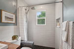 Full bathroom featuring tiled shower, toilet, tile walls, and vanity