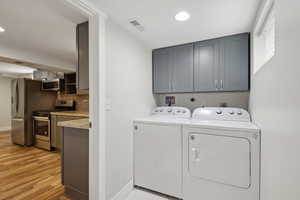 Clothes washing area featuring washing machine and dryer, light wood-type flooring, baseboards, cabinet space, and recessed lighting