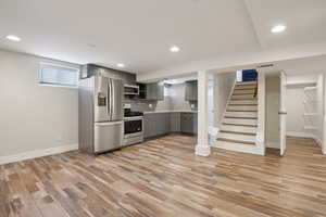 Kitchen with stainless steel appliances, gray cabinetry, ventilation hood, light wood finished floors, and recessed lighting