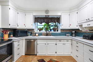 Kitchen with appliances with stainless steel finishes, a sink, light countertops, tasteful backsplash, and ornamental molding