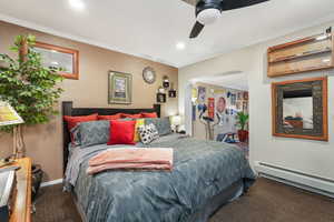 Carpeted bedroom featuring a baseboard radiator, arched walkways, ornamental molding, ceiling fan, and a textured wall