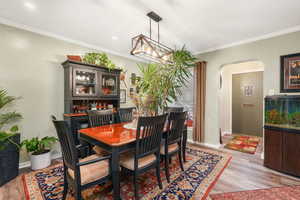 Dining area featuring arched walkways, light wood-type flooring, ornamental molding, and baseboards