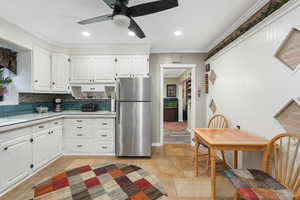 Kitchen featuring freestanding refrigerator, ornamental molding, light countertops, stone tile flooring, and backsplash