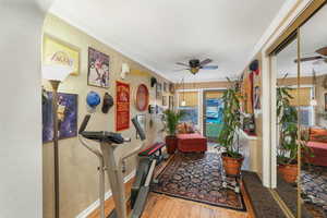 Workout room featuring a ceiling fan, wood-type flooring, crown molding, a textured wall, and baseboards