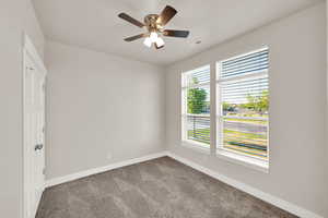 Carpeted empty room featuring baseboards and a ceiling fan