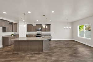 Kitchen featuring stainless steel appliances, recessed lighting, baseboards, a kitchen island with sink, and light stone counters