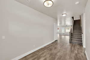Unfurnished room featuring baseboards, stairway, dark wood-style floors, and a smoke detector