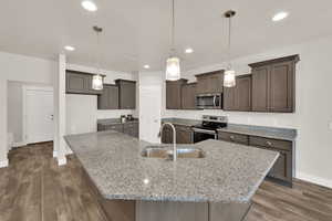 Kitchen with stainless steel appliances, a sink, baseboards, dark brown cabinetry, and a spacious island