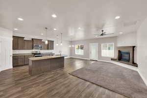 Kitchen with appliances with stainless steel finishes, recessed lighting, baseboards, a kitchen island with sink, and a glass covered fireplace
