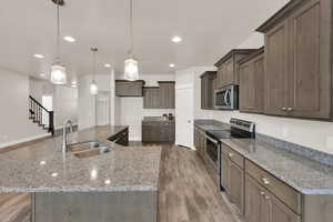 Kitchen with appliances with stainless steel finishes, a sink, light wood finished floors, recessed lighting, and a spacious island