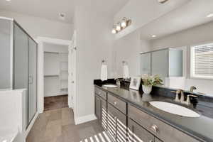 Bathroom featuring a shower stall, double vanity, a walk in closet, and baseboards