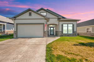 View of front of house featuring concrete driveway, a garage, a yard, board and batten siding, and stone siding