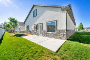 Rear view of house with stucco siding, a patio, and stone siding