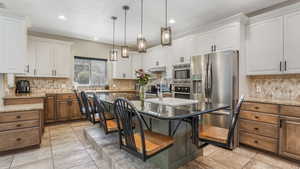 Kitchen featuring appliances with stainless steel finishes, white cabinetry, backsplash, light stone countertops, and recessed lighting