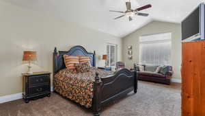 Carpeted bedroom with vaulted ceiling, baseboards, and a ceiling fan