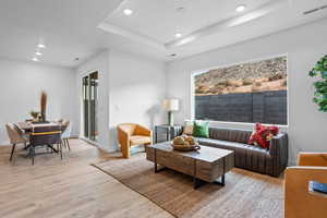 Living room featuring recessed lighting, light wood-type flooring, a tray ceiling, and baseboards