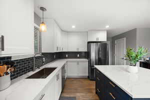 Kitchen featuring freestanding refrigerator, a sink, white cabinetry, wood finished floors, and dishwashing machine