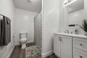 Full bathroom featuring wood finished floors, toilet, vanity, and baseboards