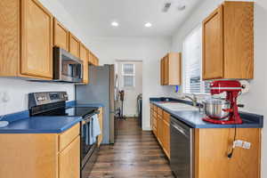 Kitchen with stainless steel appliances, a sink, dark wood-type flooring, dark countertops, and recessed lighting