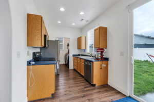 Kitchen with appliances with stainless steel finishes, a sink, washing machine and clothes dryer, dark wood-style floors, and dark countertops