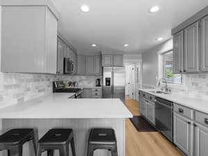 Kitchen with appliances with stainless steel finishes, a sink, gray cabinetry, light wood finished floors, and a kitchen breakfast bar