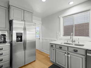 Kitchen featuring stainless steel appliances, gray cabinets, a sink, light wood-type flooring, and wainscoting