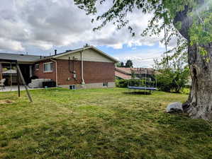 Rear view of house featuring an outdoor hangout area, a trampoline, brick siding, a patio area, and a yard