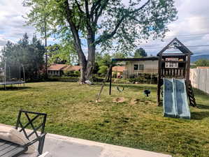 View of grassy yard featuring a trampoline and a playground