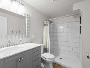 Bathroom featuring toilet, vanity, a tile shower, and wood finished floors