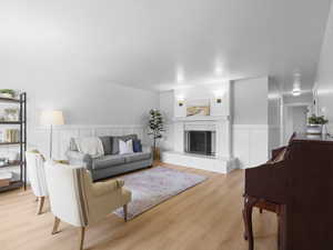Living room featuring light wood-type flooring, wainscoting, a decorative wall, and a fireplace