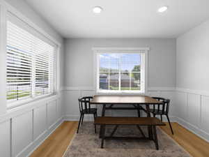 Dining room featuring healthy amount of natural light, wainscoting, light wood-style floors, recessed lighting, and a decorative wall