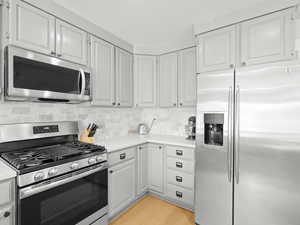 Kitchen with appliances with stainless steel finishes, light countertops, light wood-type flooring, backsplash, and white cabinets
