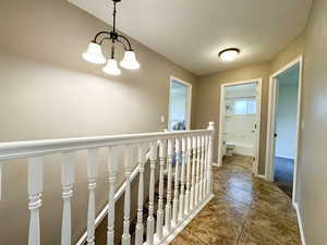 Corridor featuring a chandelier, an upstairs landing, tile patterned flooring, and baseboards