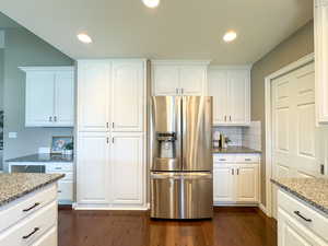 Kitchen with stainless steel fridge with ice dispenser, dark wood finished floors, light stone counters, white cabinetry, and recessed lighting