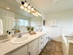 Full bath featuring a garden tub, double vanity, toilet, and baseboards