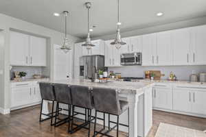 Kitchen featuring appliances with stainless steel finishes, a kitchen island with sink, decorative backsplash, dark wood finished floors, and a breakfast bar