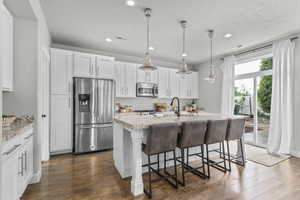 Kitchen with stainless steel appliances, dark wood-type flooring, recessed lighting, and light stone counters