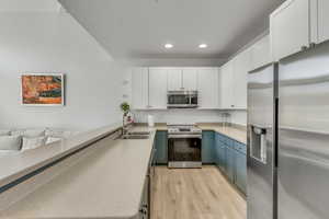 Kitchen featuring appliances with stainless steel finishes, recessed lighting, white cabinetry, light wood-style flooring, and light countertops
