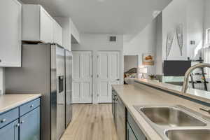 Kitchen with appliances with stainless steel finishes, light wood finished floors, blue cabinetry, light countertops, and white cabinets