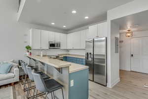 Kitchen featuring appliances with stainless steel finishes, a peninsula, a kitchen bar, blue cabinetry, and recessed lighting
