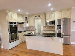 Kitchen featuring cream cabinets, stainless steel appliances, a sink, dark countertops, and light wood-style floors