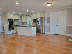 Kitchen featuring appliances with stainless steel finishes, dark countertops, cream cabinetry, light wood finished floors, and ornamental molding