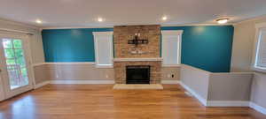 Unfurnished living room with wood finished floors, ornamental molding, a stone fireplace, baseboards, and recessed lighting