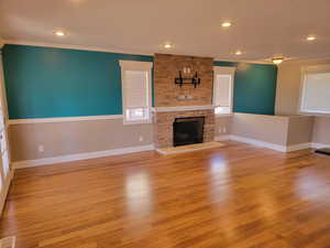 Unfurnished living room with crown molding, a fireplace, baseboards, wood finished floors, and recessed lighting