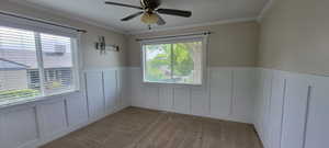 Unfurnished room with a decorative wall, wainscoting, ceiling fan, ornamental molding, and light colored carpet