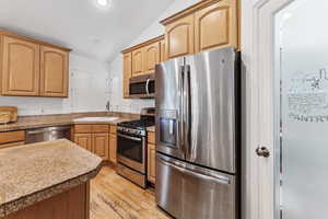 Kitchen with appliances with stainless steel finishes, a sink, vaulted ceiling, light wood finished floors, and recessed lighting
