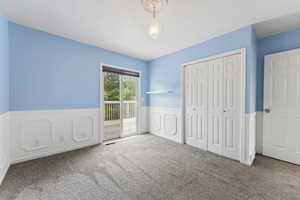 Unfurnished bedroom with carpet, access to exterior, a wainscoted wall, and a closet