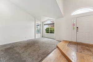 Carpeted foyer with hardwood / wood-style flooring, baseboards, and high vaulted ceiling